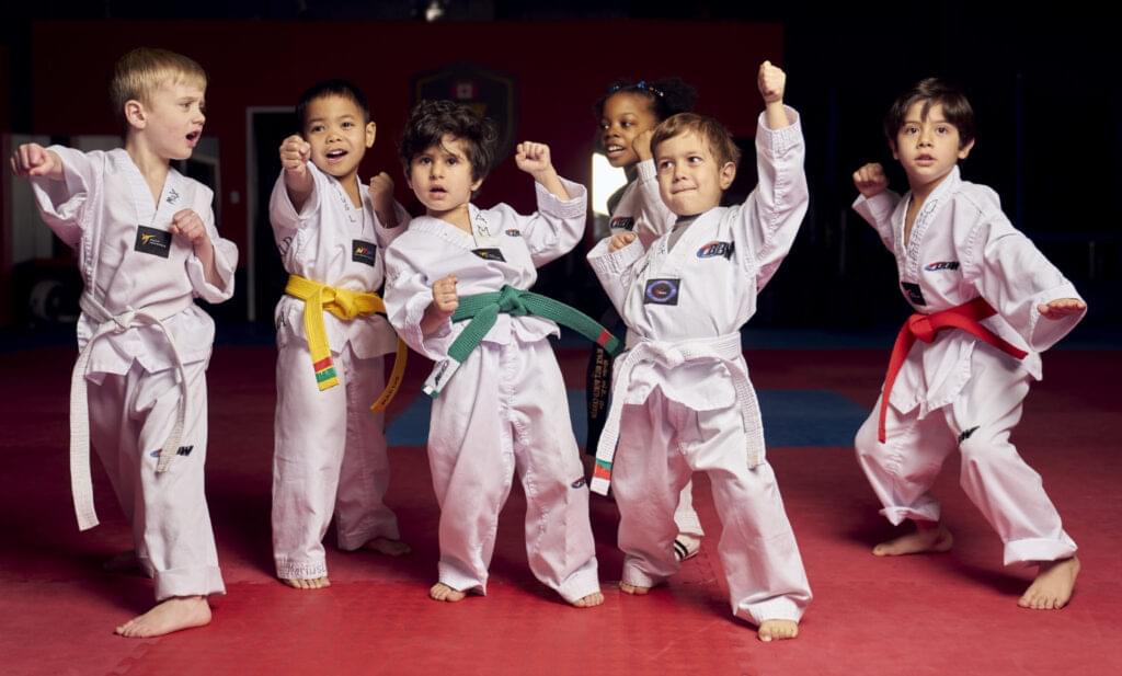 A diverse group of junior martial arts students in white uniforms performing a powerful kihap shout during their martial arts for kids session to build self confidence.