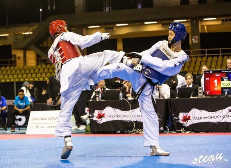 Advanced martial artists wearing electronic protective gear demonstrating high-level point-scoring kicks during an official tournament match.