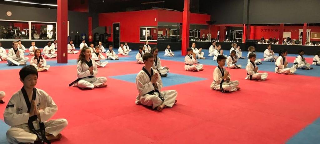 A large group of students in a professional martial arts dojang practicing seated meditation to improve mental focus and discipline.