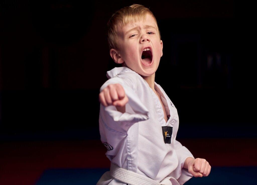 A determined young student in a clean white uniform practicing white belt basics with a powerful straight punch and intense martial arts focus.