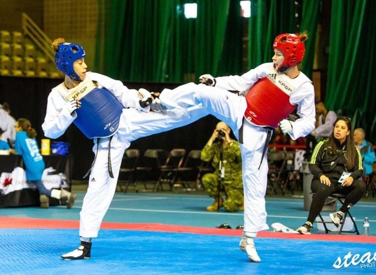 Two female athletes competing in a high-intensity taekwondo match to demonstrate female empowerment and technical skill.