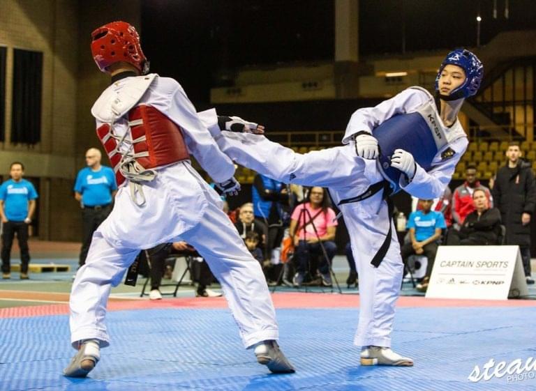 Two advanced athletes wearing protective gear while performing a tactical roundhouse kick during an official Taekwondo match.