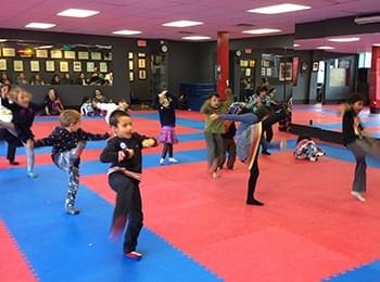 Young students practicing taekwondo balance drills on professional martial arts mats to improve core stability.